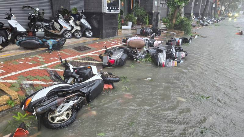 昨（25日）高雄市三民區同盟路一帶路面積淹水，機車被吹倒、泡在水裡。圖/中央社