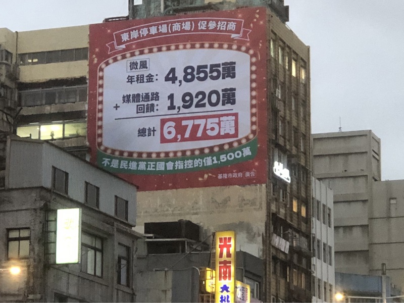 基隆市政府24日在忠一路大樓外牆高掛起巨幅廣告，提到「東岸停車場（商場）促參招商」收入 數據。圖/中央社