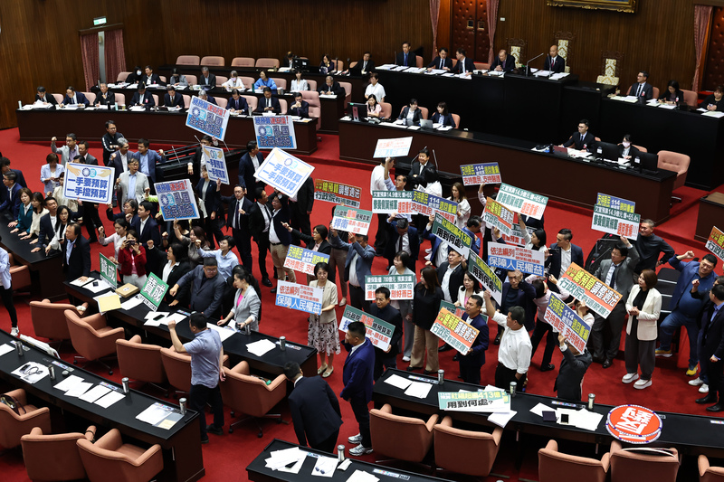 114年中央政府總預算案日前在立法院會遭藍白聯手退回程序委員會，但民進黨團在18日院會仍透過議事攻防，積極爭取儘早排審總預算案的機會。圖為民進黨立委在議場內高舉看板呼口號表達立場。圖／中央社