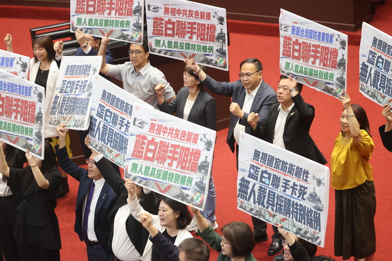 立法院正在處理行政院提出的2100億元《國防自主無人載具採購特別條例》草案，國民黨與民眾黨團在報告事項議程時提議暫緩列案，而綠委則手持標語抗議。圖/中央社